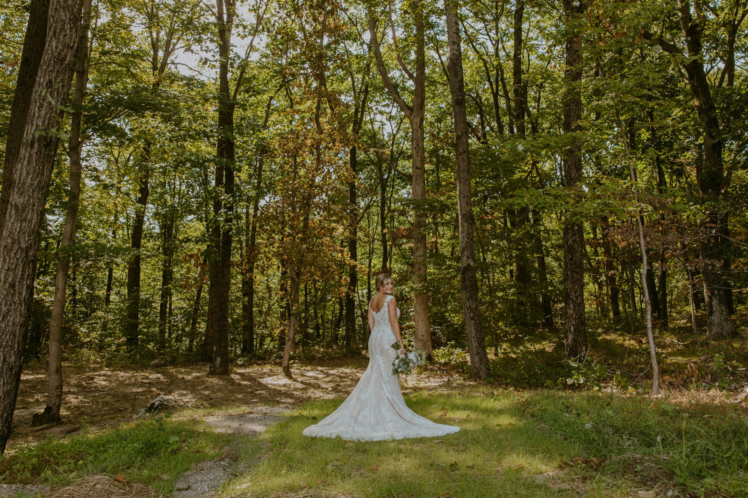 Bride stands in the middle of a lush green forest for her bridal portraits