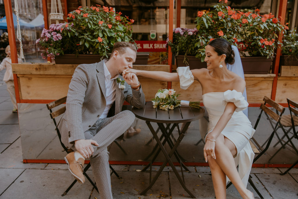 Couple sits at cafe while groom kisses brides hand.