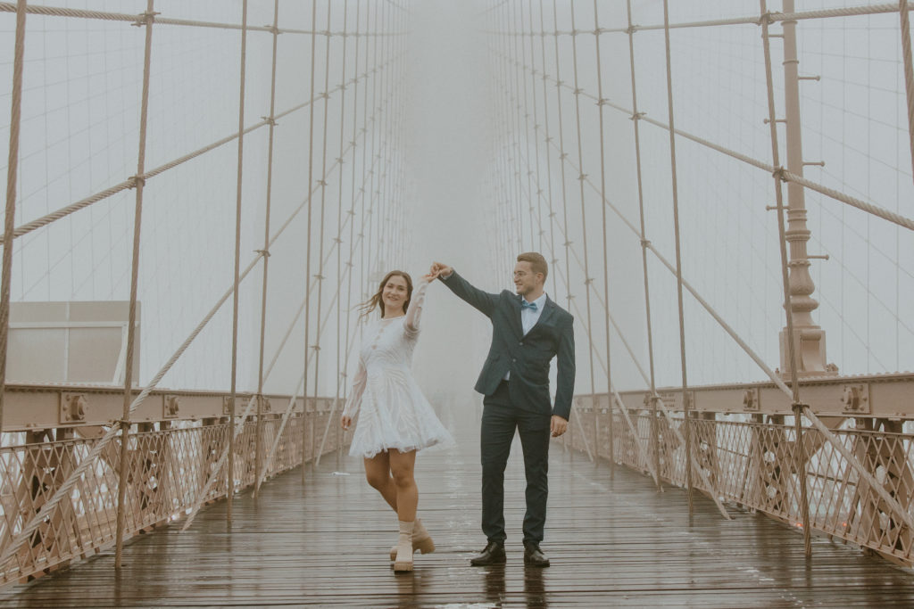 Elopement couple spins on the Brooklyn Bridge as it rains