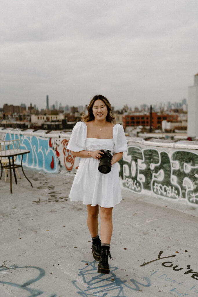 Photographer stands on Bushwick roof with manhattan skyline in the background.