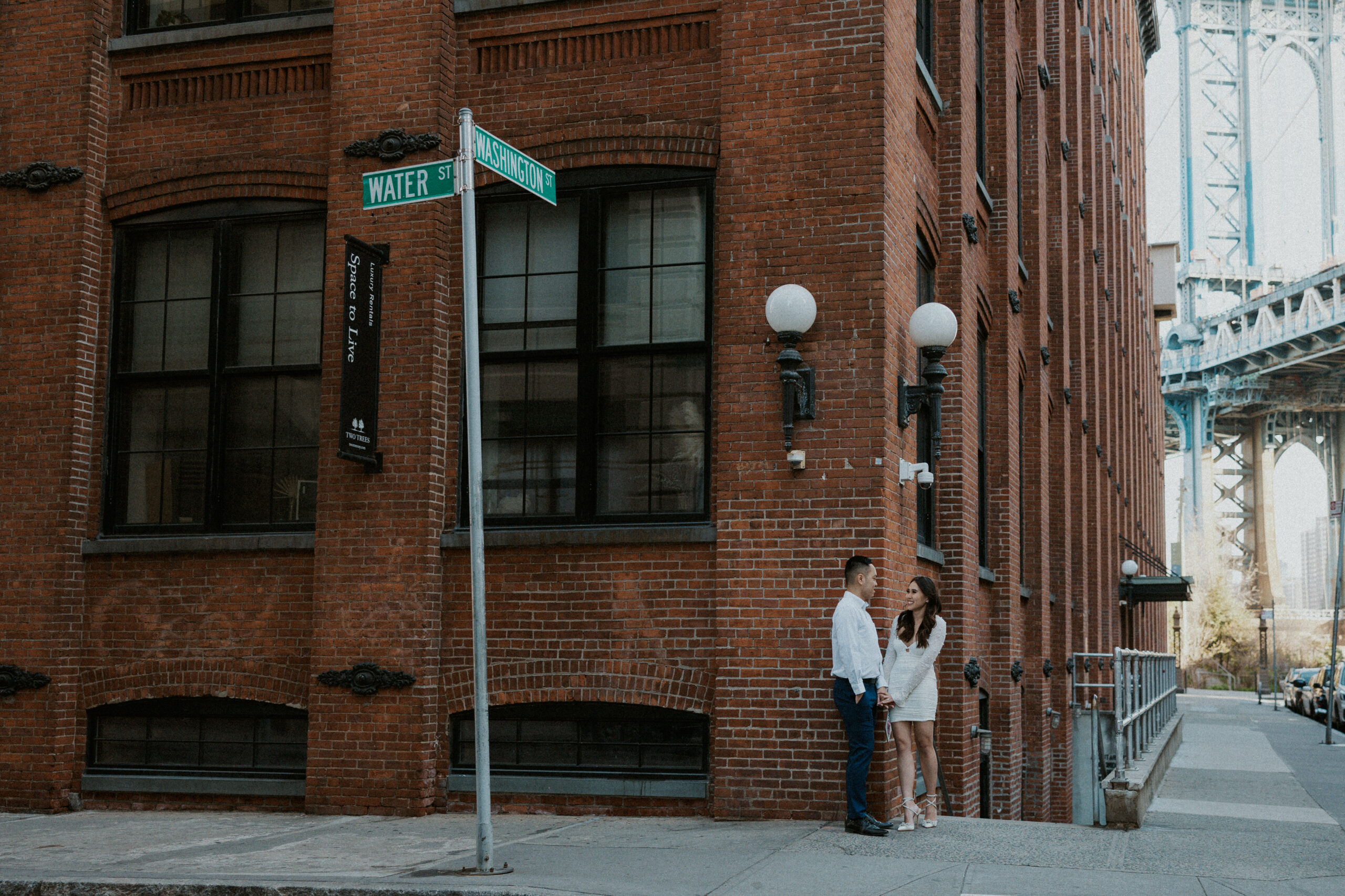 Couple stands on the corner of the sidewalk in DUMBO